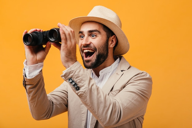 Portrait of man in hat holding binoculars on orange wall