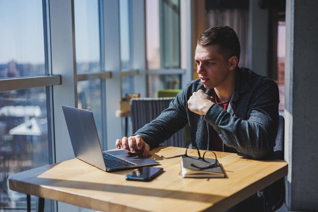 Portrait of a man IT professional working remotely with a modern laptop sitting at a table and smiling at the camera during a break a happy human programmer in vision correction glasses