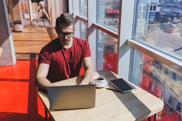 Portrait of a man IT professional working remotely with a modern laptop sitting at a table and smiling at the camera during a break a happy human programmer in vision correction glasses