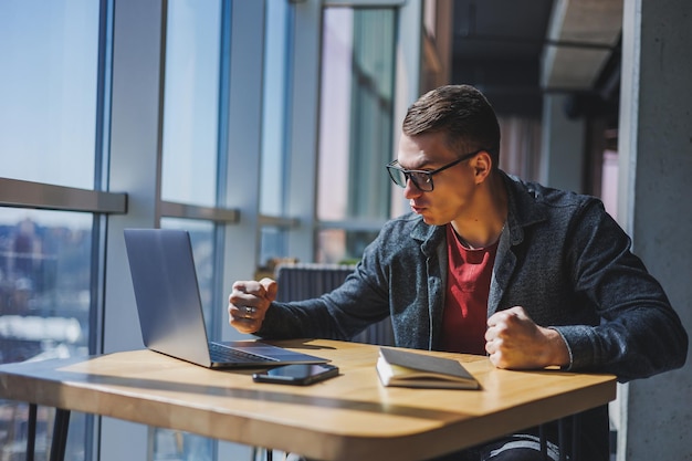 Portrait of a man IT professional working remotely with a modern laptop sitting at a table and smiling at the camera during a break a happy human programmer in vision correction glasses