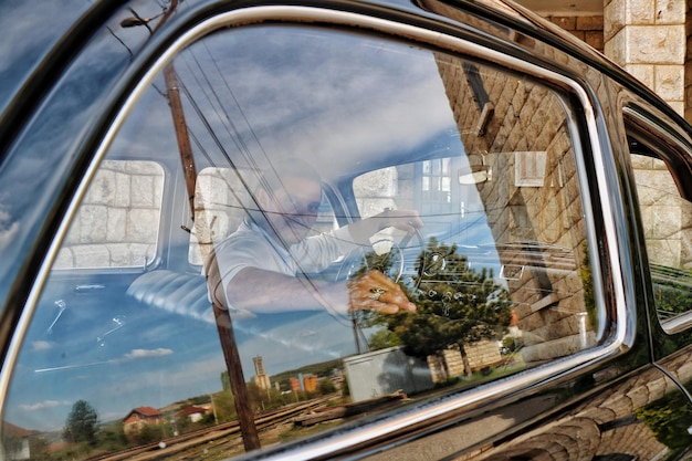 Photo portrait of man sitting in vintage car seen through window