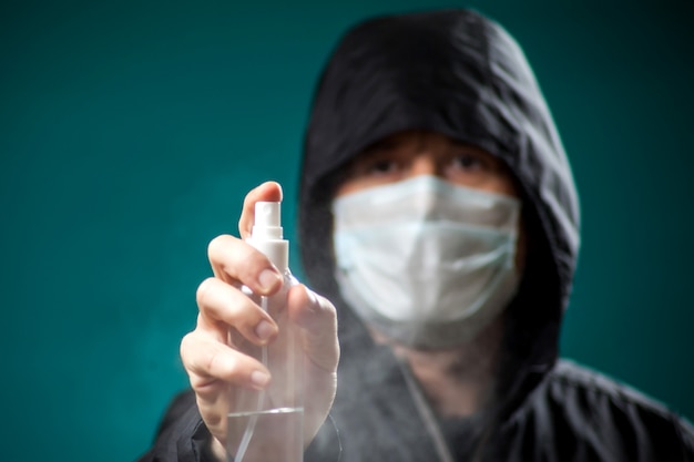 A portrait of man with medical face mask showing disinfectant spray at camera. People, medicine and healthcare concept. Coronavirus protection