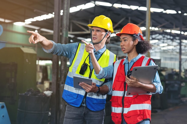 A portrait of a manufacturing worker in discussion with an industrial man and woman engineer holding a tablet in a factory. A Caucasian foreman is in supervision of a CNC machine.