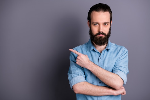 Portrait of masculine brutal bearded guy point index finger copy space indicate promo adverts present advertisements suggest select wear casual style outfit isolated grey color wall