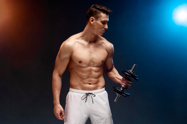 Portrait of masculine young man holding dumbbell isolated on black background