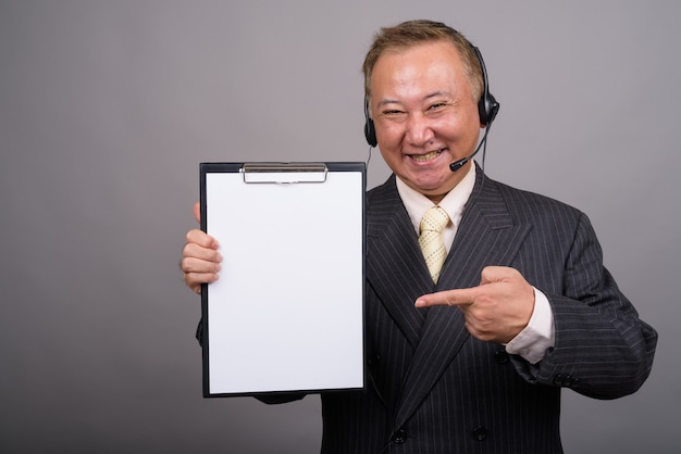 Portrait of mature Asian businessman against gray wall