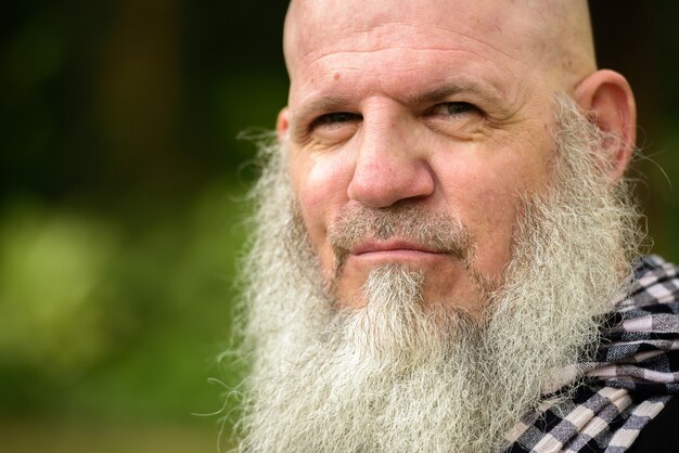 Portrait of mature bald hipster man with long beard at the park outdoors