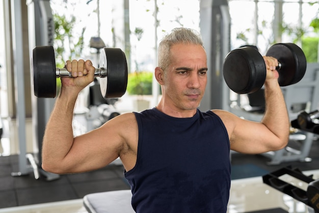 Portrait of mature handsome Persian man with gray hair exercising at the gym