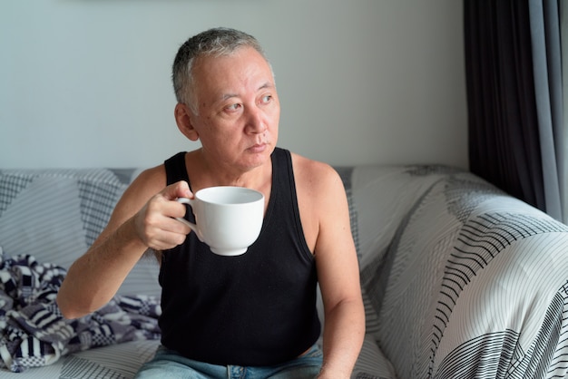 Portrait of mature Japanese man drinking coffee and thinking in the living room