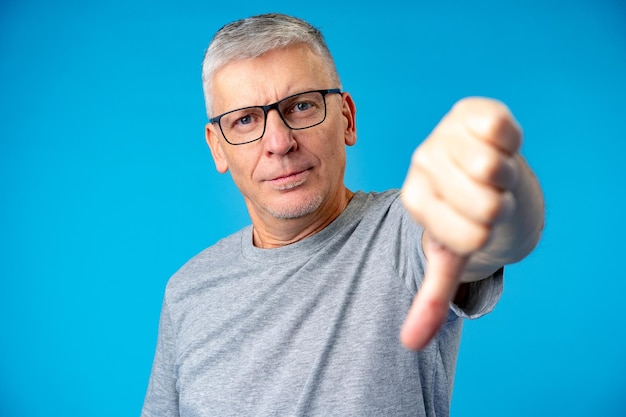 Portrait of mature man showing thumbs down sign gesture standing on blue backgorund