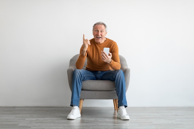 Portrait of mature man using smartphone sitting on armchair