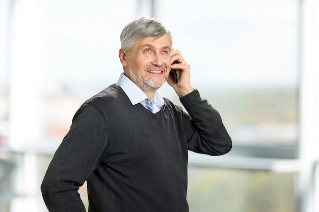 Portrait of mature man with phone. Smiling senior man with phone smiling and looking upwards.