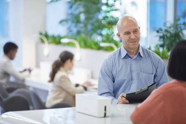 Portrait of mature manager smiling at client or customer while standing at reception desk