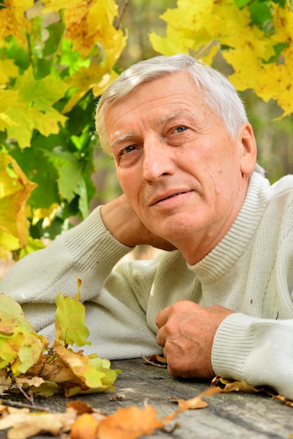 Portrait of mature thoughtful man sitting at table outdoors over autumn background