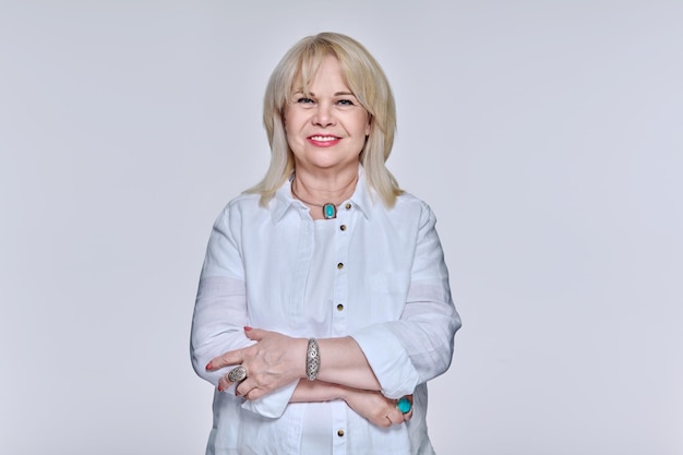 Portrait of mature woman in glasses looking at camera on light background