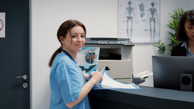 Portrait of medical assistant talking to receptionist at hospital reception counter, having conversation in waiting area lobby. Nurse and secretary working in healthcare support.