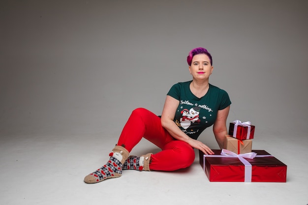 Portrait of meditating relaxed woman with dyed purple hair sitting on the floor with crossed arms balancing wrapped Christmas presents on hands