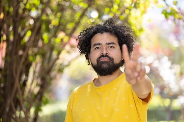 Portrait of a Mexican man smiling with curly hair and beard making peace sign