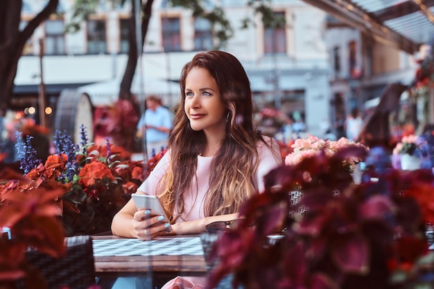 Portrait of a middle age businesswoman with long brown hair holds a smartphone while sitting at an outdoor cafe.