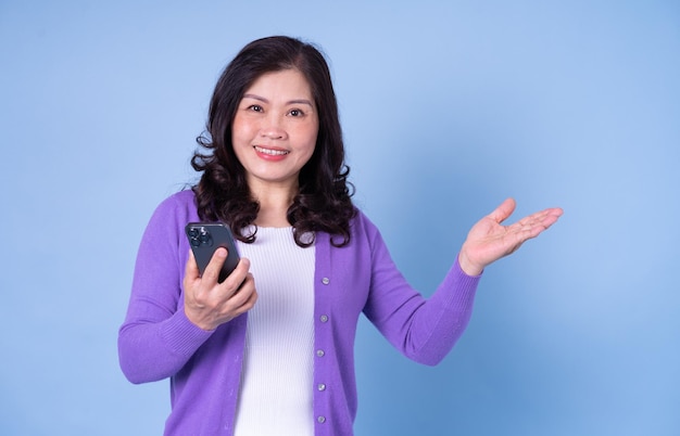 Portrait of middle aged Asian woman using smartphone on blue background