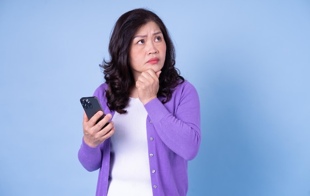 Portrait of middle aged Asian woman using smartphone on blue background