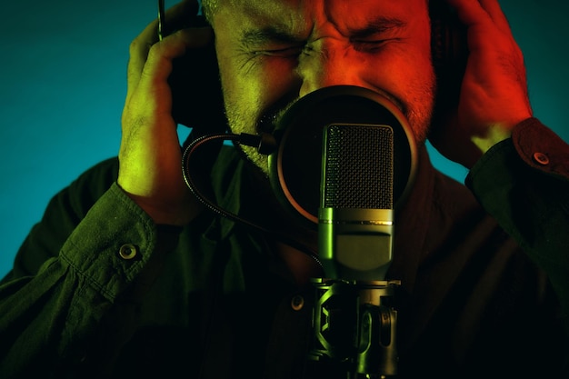 Portrait of a middle aged man wearing headphones and singing into a microphone isolated on green background close up look