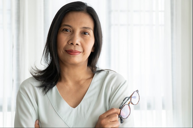 Portrait of middle aged smiling woman holding glasses at home