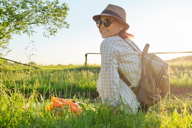 Portrait of middle-aged woman in sunglasses with hat with backpack, relaxing in nature