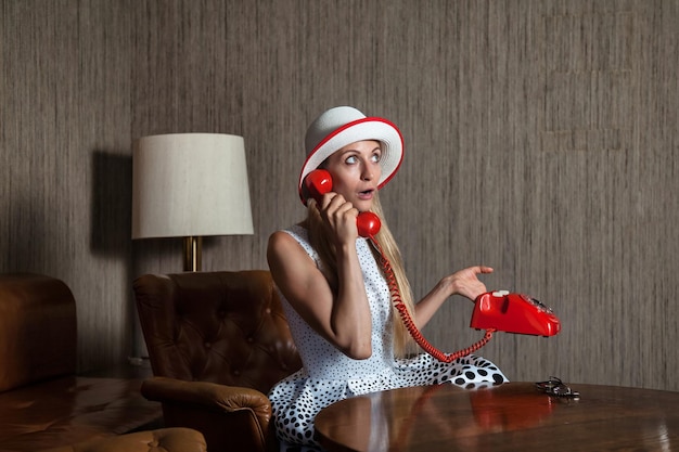 Portrait middle aged woman talking on red fixed land line telephone in vintage interior living room