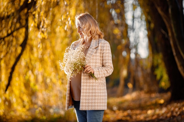 Portrait of middleaged pregnant woman outdoors at park Middle age pregnant woman expecting baby at aged pregnancy Blonde woman wearing brown sweater and beige coat