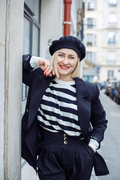 Portrait of middleaged smiling woman with short fair hair red lipstick wearing black pants suit standing on street