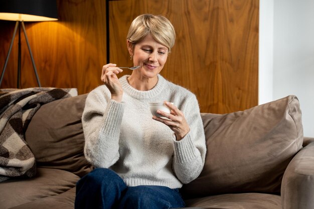 Portrait of a middleaged woman who eats yogurt sitting on the couch at home