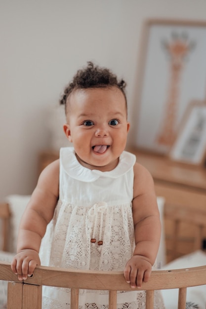 Portrait of mixed race toddler girl in round wooden baby crib at cozy childrens room neutral tones