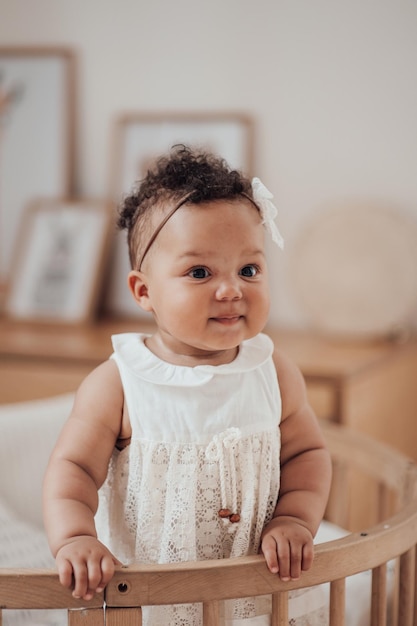 Portrait of mixed race toddler girl in round wooden baby crib at cozy childrens room neutral tones