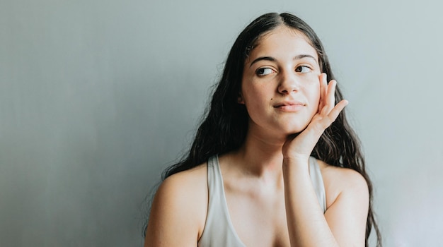 Portrait of model with hand in face relaxed after dermatology skin treatment Young adult woman skincare glow from spa rituals posing with glowing clean and clear skin and no makeup