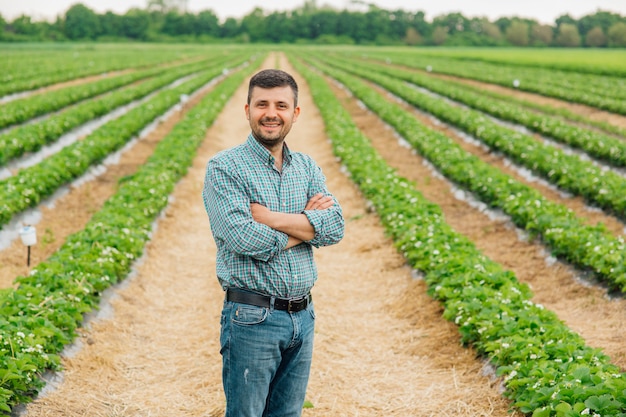 Portrait of a modern bearded farmer man with crossed arms looking at camera stands in the agricultural field cheerful male worker in agricultural farm agriculture farming