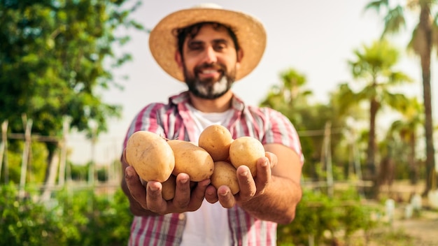 Portrait of a modern bearded farmer man with potatoes on hands looking at camera