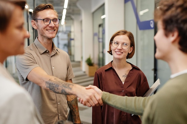 Photo portrait of modern business team welcoming new employee focus on smiling tattooed man shaking hands with intern