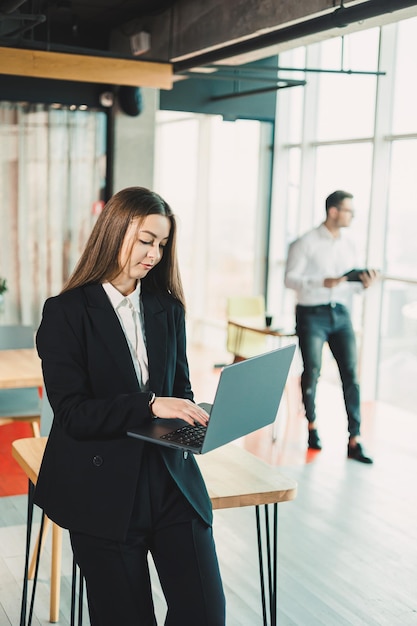 Portrait of a modern business woman with a laptop in the office A business woman in a black classic suit who works online in the office