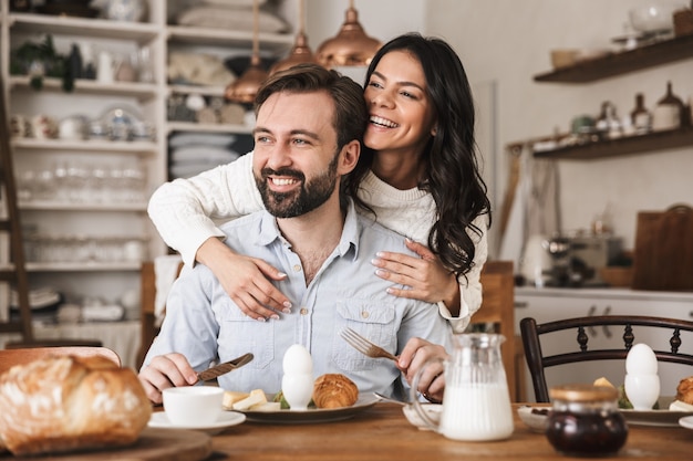 Portrait of modern european couple man and woman eating at table while having breakfast in kitchen at home