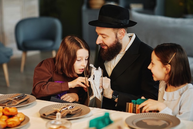 Portrait of modern jewish family sharing presents with children at dinner table in cozy home setting