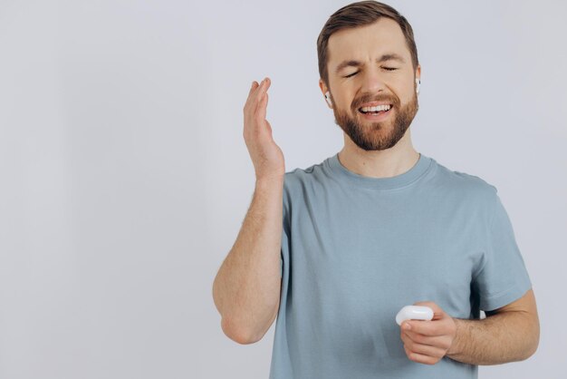 Portrait of modern millennial man with beard holding wireless earphones on white background with copy space