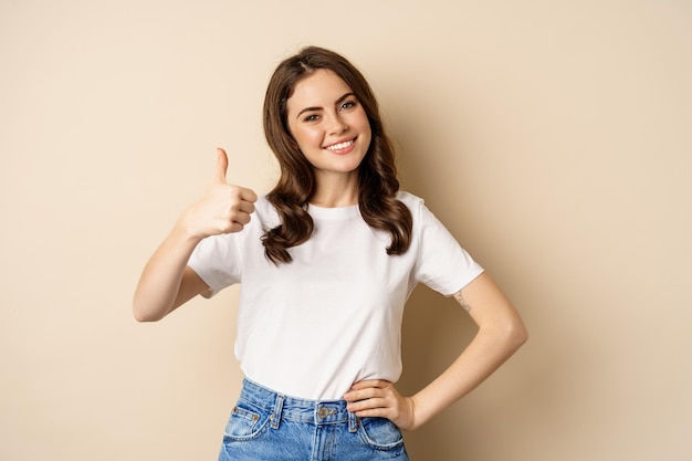 Portrait of modern young woman showing thumbs up like and approve smiling pleased recommending compa...