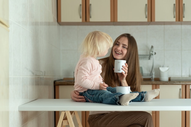 Portrait of mom and baby in kitchen. Happy young mom and toddler have breakfast at home.