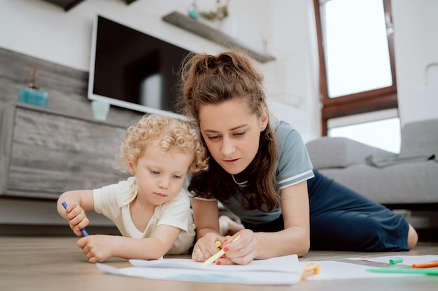 Portrait of mom with her preschoolaged daughter spending their free time drawing together while lyin