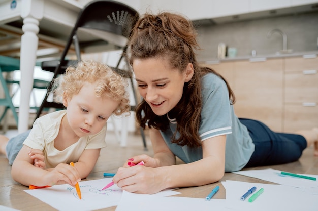 Portrait of mom with her preschoolaged daughter spending their free time drawing together while sitt