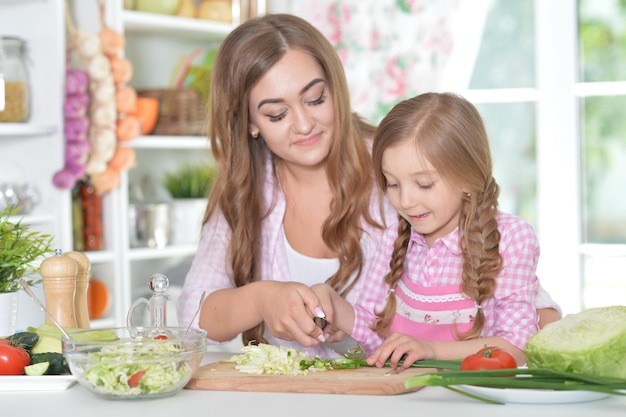 Portrait of mother and daughter preparing salad on kitchen together