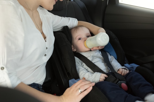 Portrait of mother giving her baby milk on car back seat