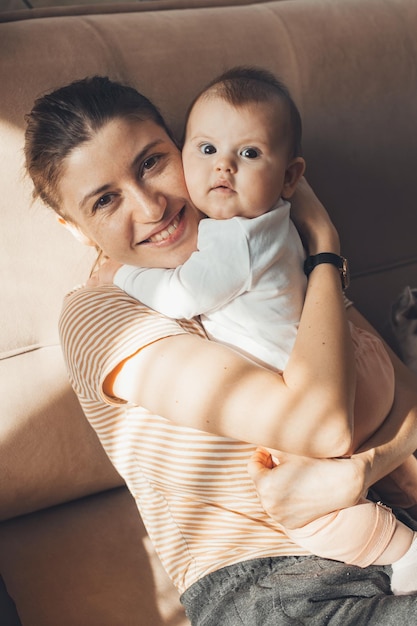 Portrait of a mother hugging her cute baby child sitting on sofa little girl sitting in mother arms