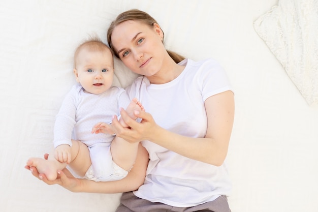 Portrait of a mother with a baby in her arms gently embracing him on a white bed at home, mother's love